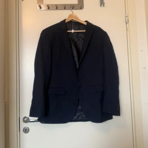 Mörkblå kavaj från Matinique - Säljer en klassisk mörkblå kavaj från Matinique i storlek 50. Kavajen har två knappar framtill, fickor med lock och en innerficka. Perfekt för dig som vill ha en stilren och tidlös look. Vet inte om det är en dam eller her T-modell. Använd av kvinna i storlek XL/ XXL. Mycket fint skick, jag hittar inga synliga anmärkningar eller defekter. 