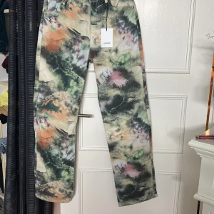 Flerfärgade Spray Jeans från Junkyard - Unika jeans från Junkyard med sprayfärgat mönster i grönt, rosa, orange och svart. Byxorna har raka ben, klassisk femficksdesign och normal passform. Perfekta för dig som vill sticka ut med din stil.