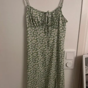 Grön blommig klänning med smala axelband från SHEIN - Söt grön klänning från SHEIN med små vita och röda blommor, smala axelband och knytning framtill vid bysten. Lätt och luftig modell som passar perfekt till varma dagar.