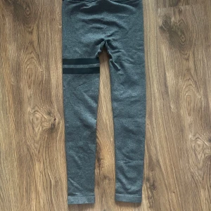 Grå leggings från Stronger med svarta ränder - Mörkgrå leggings från Stronger med två svarta ränder runt ena låret. Hög midja och stretchigt material som sitter tight. Perfekta för träning! 💓