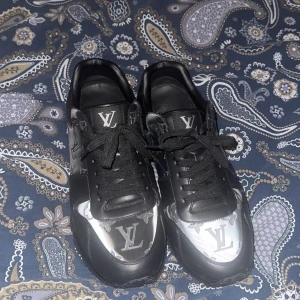 Svarta Louis Vuitton sneakers med monogram - Säljer ett par svarta Louis Vuitton sneakers med klassiskt LV-monogram i grått och silver på ovandelen. Skorna har snörning, rund tå och platt sula. Snygg och modern design med exklusiv känsla. Storlek 43, passar dock 42 med.  Box och allting finns till skorna!