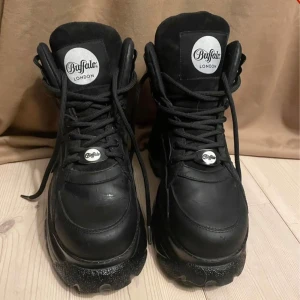 Buffalo London svarta platåsneakers - Buffalo London sneakers i helsvart skinn med kraftig platåsula och snörning. Ikonisk logga på plös och häl. Snygga skor som sticker ut. Finns att hämta i Kalmar. Ska de skickas står köparen för frakten :)