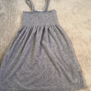 Grå klänning med smock från Juicy Couture - Supersöt grå klänning från Juicy Couture med smock upptill och tunna axelband. Mjuk och bekväm, perfekt för varma dagar. Funkar även som strand klänning. Köpt för 600kr, och helt oanvänd.💕