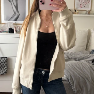 Beige bomberjacka med dragkedja - Säljer en stilren beige bomberjacka med dragkedja framtill. Jackan har lång ärm, ribbade muddar och klassisk bomberkrage. Perfekt för dig som vill ha en enkel och snygg jacka till vardags. Har en liten sminkfläck på ena mudden på armen, går säkert bort i tvätt 💗