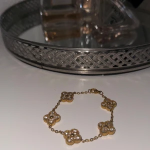 Guldigt armband med fyrklöverdesign - Säljer ett elegant armband i guldton med flera fyrklöverformade länkar. Varje länk har en detaljerad, pärlliknande kant som ger ett lyxigt intryck. Perfekt accessoar för att lyfta din outfit.