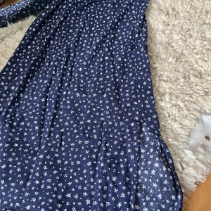 Mörkblå blommig klänning från H&M - Söt mörkblå kjol från H&M med små vita blommor över hela tyget. Mjuk och lätt i materialet, passar både till vardags och speciella tillfällen.