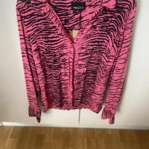Rosa zebramönstrad skjorta från pieces - Säljer en rosa skjorta set från pieces  med svart/rosa zebramönster. Skjortan har långa ärmar, klassisk krage och knäppning framtill. Perfekt statement-plagg för dig som vill sticka ut med färg och mönster. Matchande byxor till high waist , loose fit. Prislappar kvar 449 kr styck säljer båda för 400 kr stl xs/s