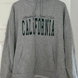 Grå Hoodie med tryck från Lager 157 - Grå hoodie, med mörk grönt Carlifonia tryck. Från lager 157 manavdelningen 