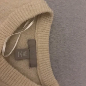 Beige kofta från H&M - Mysig beige kofta från H&M med rund halsringning och knäppning framtill. Tröjan har långa ärmar och breda ribbade muddar vid ärmslut och nederkant. Perfekt för lager-på-lager och enkel att matcha med olika outfits.