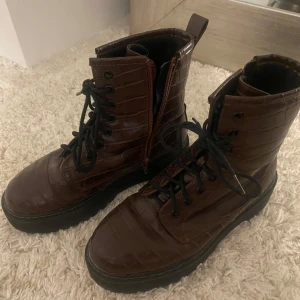 Bruna boots med snörning - Snygga bruna boots med krokodilmönster och snörning. De har en dragkedja på sidan för enkel på- och avtagning. Perfekta för en cool och trendig look.