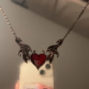 Halsband med rött hjärta och vingar - Unikt halsband med ett rött hjärta i mitten och detaljerade vingar på sidorna. Kedjan är i en mörkare metallfärg som ger en gotisk känsla. Fråga ifall du undrar något 🩷Perfekt för att lagra med andra halsband. Ordinarie pris 129kr.