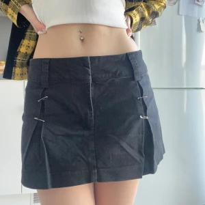 Svart kortkjol med säkerhetsnålar - Snygg svart lågmidjad kortkjol. Jeans aktigt material. Tar ut säkerhetsnålarna innan jag skickar! Har satt dit dom själv