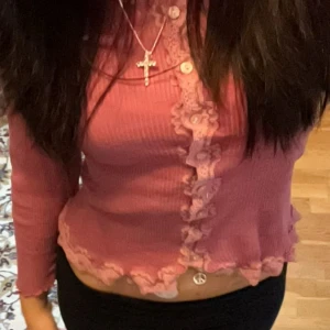 Rosa ribbad kofta från Rosemunde - Säljer en söt rosa ribbad kofta från Rosemunde med spetsdetaljer längs kanterna och knappar framtill. Koftan har långa ärmar och en v-ringad design. 