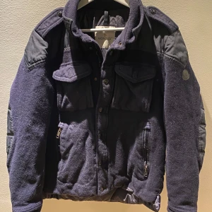 ÄKTA  Moncler jacka  - Säljer en snygg mörkblå jacka från Moncler med quiltade detaljer och dragkedjor. Jackan har långa ärmar och flera fickor framtill. Perfekt till våren. Jackan är i bra kvalitet bara att dragkedjan är sönder men det finns knappar. Storlek 3 men passar bättre till 2