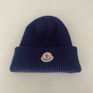 Mörkblå ribbad mössa från Moncler - Snygg mörkblå ribbad mössa från Moncler med broderad logotyp framtill. Mössan är i nyskick och har inga tecken på användning, har tyvärr ingen prislapp eller ordinarieförpackning. Kom gärna med prisförslag.
