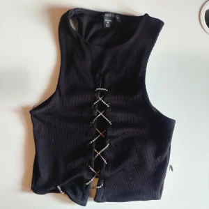 Svart ribbad linnetopp med snörning - Snygg svart ribbad linnetopp med cool snörning framtill. Perfekt för en trendig look. Passar bra till både jeans och kjol. 🖤    Jag skulle nog säga att den ger av en club känsla, är öppen i mitten för en lite exposed känsla. Den är XS men fick plats på mig som är M till L.