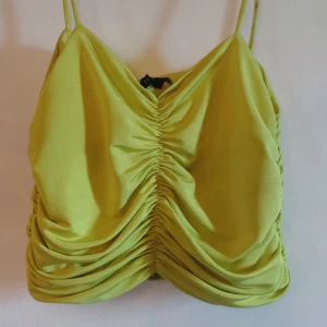 Grön draperad linnetopp - Snygg grön linnetopp med smala axelband och draperad design. Perfekt för en somrig look med en unik stil. Toppen har en åtsittande passform och är tillverkad i ett mjukt material.