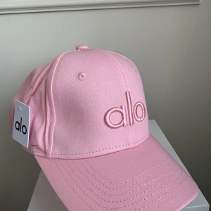 Rosa keps från Alo - Snygg rosa keps från Alo med broderad logga framtill. Perfekt för en avslappnad stil. Justerbar passform för extra komfort.