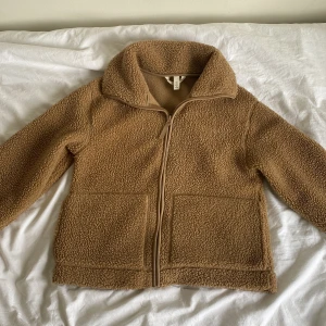 Beige teddyjacka med dragkedja - Mysig beige teddyjacka med dragkedja framtill och stora fickor.  Jackan har en hög krage och långa ärmar för extra komfort. Ser brun ut på bilden, men jackan är beige (kolla andra bilden) 