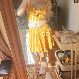 Gul- och vitrandig topp och kjol - Säljer en somrig gul- och vitrandig set med en söt knyt-topp och matchande kjol. Toppen har smala axelband och en knytning framtill, medan kjolen är kort och fladdrig. Perfekt för soliga dagar!