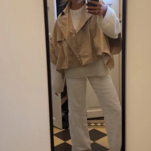 Beige  trenchcoat - Säljer en beige croppad trenchcoat med dubbelknäppning. Jackan har en lös passform och är perfekt för lager-på-lager-stil. Den är stilren och lätt att matcha med olika outfits. Från cos! One size