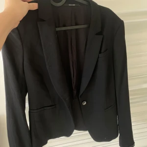 Svart kavaj från Tiger of Sweden - Snygg svart kavaj från Tiger of Sweden. Perfekt för en stilren look med klassisk design och enkel knapp framtill. Passar bra till både formella och semi-formella tillfällen.
