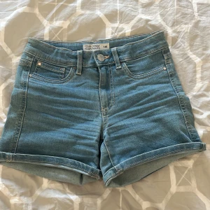 Blå jeansshorts från Cubus  - Snygga blå jeansshorts från Cubus. De har en klassisk femficksdesign och uppvikta benslut för en avslappnad look. Perfekta för varma dagar!