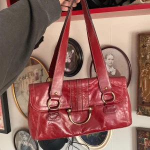 Röd axelväska i skinn - cute och chic röd axelväska i äkta skinn med guldfärgade detaljer. köpt på loppis, aldrig använd. 