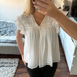 Vit blus med volangdetaljer - Säljer en söt vit blus med volangdetaljer på ärmarna, från Gina Young. Blusen har en v-ringad design och är tillverkad i ett lätt och luftigt material, perfekt för varmare dagar. Passar bra till både jeans och kjol.