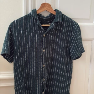 Randig kortärmad skjorta från Zara - Snygg randig skjorta från Zara i mörkgrön och vit. Skjortan har korta ärmar och knappar framtill. Perfekt för en avslappnad stil.