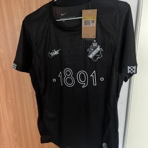 AIK smoking lirare!Svart fotbollströja med tryck 1891 - Snygg svart fotbollströja från Nike med trycket '1891' på framsidan och nummer '10' på baksidan. Tröjan har korta ärmar och ett stilrent klubbemblem på bröstet. Perfekt för fotbollsfans som vill visa sitt stöd.