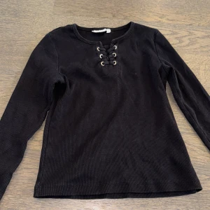 Svart ribbad tröja från KappAhl - Säljer en svart ribbad tröja från KappAhl med snörning framtill. Tröjan har långa ärmar och en stilren design som passar perfekt till vardags. Perfekt för höst och vinter!(första bilden var med blixt och inte de andra!🩷