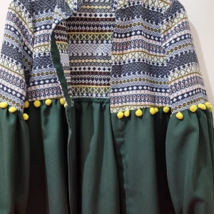 Mönstrad jacka med gröna ärmar och gula detaljer - Unik jacka med ett färgglatt mönster i blått, vitt och grönt på överdelen och mörkgröna ärmar. Jackan har långa ärmar och är dekorerad med gula bollar längs ärmslutet.