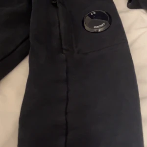 Svart tröja från C.P. Company - Säljer en stilren svart tröja från C.P. Company med en unik detalj på ärmen. Tröjan har långa ärmar och en normal passform, perfekt för en avslappnad look. Passar bra till jeans eller chinos. Storlek M passar även S, jag är öppen för prisförslag så bara skicka!