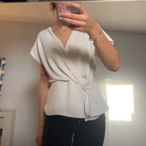 Vit omlottblus zara - Säljer en elegant vit omlottblus med korta ärmar och knytning i midjan. Perfekt för en stilren look. Blusen har en v-ringad design som ger en feminin touch💕💕