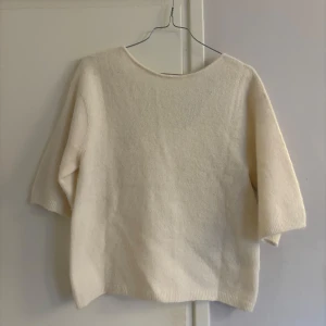 Vit kortärmad stickad tröja från ARKET - Super söt vit stickad tröja från ARKET, fin detalj med v-ringad i ryggen🌸 storlek XS, lösare modell, använd 1 gång på jobbet. Ull och alpacka blandning. Tror nypris var 790kr eller 990kr.