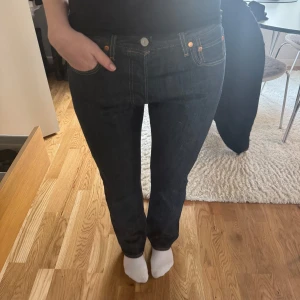 Mörkblå jeans från Levis - Snygga mörkblå jeans från Levis med klassisk femficksdesign och knappgylf. Jeansen har en rak passform och är perfekta för en avslappnad stil. De har också de ikoniska Levis-detaljerna som läderpatch och röda etiketten på bakfickan. Nästan aldrig använda, säljer då de är lite korta i längden. (Köpta för ca 1200kr)