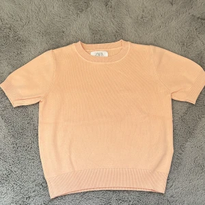 Persikofärgad kortärmad tröja från Zara - Säljer en söt persikofärgad tröja från Zara. Den är kortärmad och har en ribbad struktur som ger en stilren look. Perfekt för vår och sommar! 🌸 PRIS KAN DISKUTERAS!