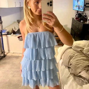 Ljusblå axelbandslös klänning - Charmig ljusblå klänning med volanger i flera lager. Den är axelbandslös och har en luftig och lekfull design, perfekt för varma dagar.
