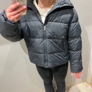 Svart pufferjacka med dragkedja - Säljer en svart pufferjacka med dragkedja. Jackan har en hög krage och långa ärmar, perfekt för kyligare dagar. Den är quiltad och ger en skön och varm känsla. Passar bra till både vardag och utflykter.