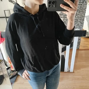 Svart hoodie - Säljer en svart hoodie med luva och dragsko. Tröjan har en bekväm passform och en praktisk magficka framtill. Perfekt för en avslappnad stil.