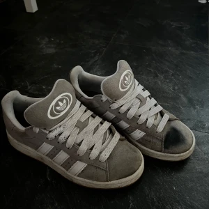 Grå Adidas sneakers - Säljer ett par grå Adidas sneakers med klassisk design och vita ränder. Som man ser så är det smuts framme på skon därför är priset sopas lågt