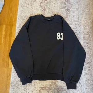 Svart sweatshirt från Gina Tricot - Säljer en svart sweatshirt från Gina Tricot med texten 'Downtown 93 Sports Club' i vitt på ryggen och siffran 93 på bröstet. Tröjan har långa ärmar och ribbade muddar vid ärmslut och nederkant. Perfekt för en avslappnad stil!