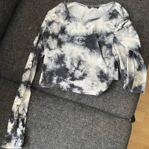 Svartvit croppad topp med knyt nere vid ryggen - Säljer en cool svartvit croppad topp med batikmönster. Toppen har långa ärmar och en knytning i ryggen som ger en unik look. 