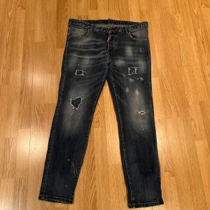 Mörkblå jeans från Dsquared2 - Mörkblå jeans från Dsquared2 med slitna detaljer. Använda 3 gånger. Köpta på NK i Göteborg för nåra år sedan. Aldrig kommit till användning. Sitter som L om man ska gå på något.