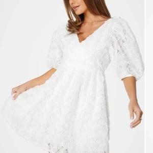 Vit spetsklänning - Charmig vit klänning med v-ringning och trekvartsärmar. Klänningen är täckt av vacker spets och har en luftig passform som ger en romantisk känsla.