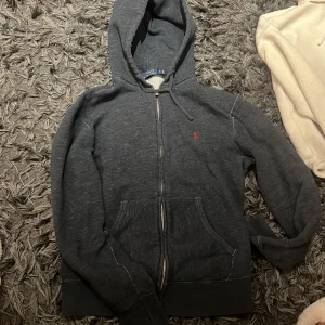 Mörkgrå hoodie från Polo Ralph Lauren - Säljer en snygg mörkgrå hoodie från Polo Ralph Lauren med dragkedja och huva. 