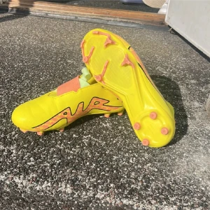 Gula fotbollsskor från Nike - Snygga gula fotbollsskor från Nike med orange och svarta detaljer. Skorna har en tight passform och är designade för optimal prestanda på planen. Perfekta för dig som vill sticka ut med stil och funktion.