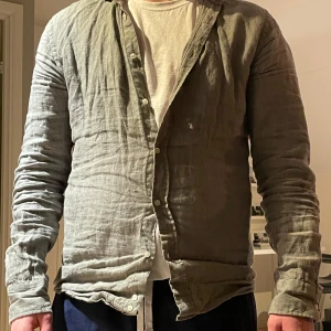 Grön linneskjorta från Bläck - Snygg grön skjorta i linne från Bläck med långärmad design och knappar framtill. Perfekt för en stilren och avslappnad look. Tailored fit för en modern passform.