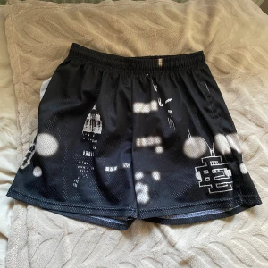 Svarta mönstrade shorts från EE - Snygga svarta shorts från EE med ett unikt mönster som påminner om en stadssilhuett. De har en elastisk midja för extra komfort och är perfekta för en avslappnad stil. Tillverkade i New York. 